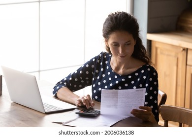 Focused young woman using calculating taxes, budget, costs, paying bill, rent or mortgage fee, checking paper invoice, receipt. Accounting professional with laptop and calculator working from home