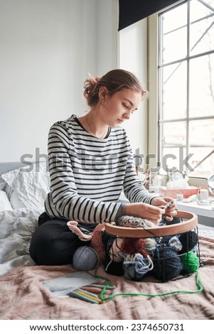Focused young woman wearing headphones knitting at the bed