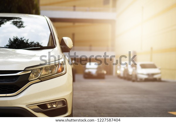 Focusing on the White car\
headlights on a street corner with sunlight flares and  small white\
car, In the background, the driver and car. Car parking on the\
street