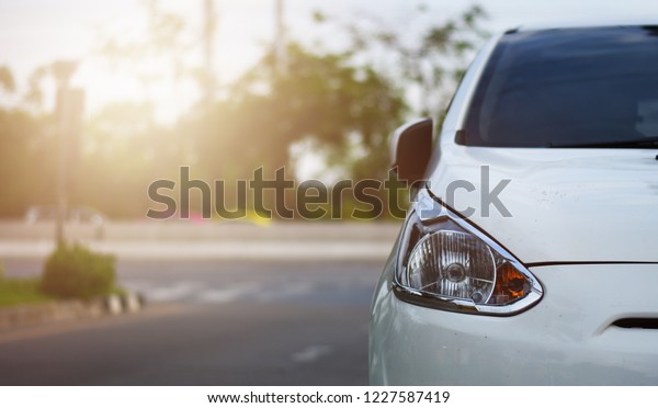 Focusing on the White car headlights on a street\
corner with sunlight flares and  small white car, In the\
background, the driver and car. Closeup headlights of car. Copy\
space for insert text.