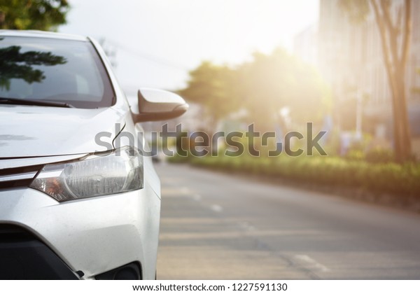 Focusing on the White car\
headlights on a street corner with sunlight flares and  small white\
car, In the background, the driver and car.  Car parking on the\
street
