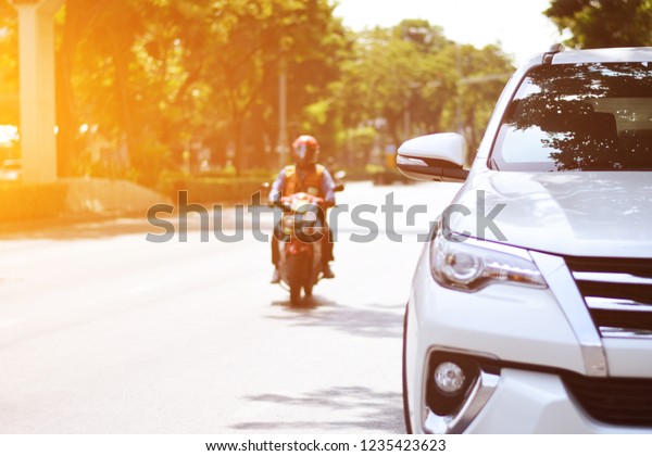 Focusing on the White car\
headlights on a street corner with sunlight flares and  small white\
car, In the background, the driver and car. Car parking on the\
street.