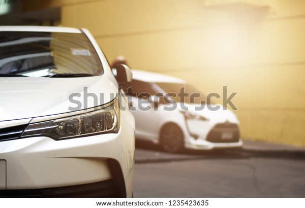 Focusing on the White car\
headlights on a street corner with sunlight flares and  small white\
car, In the background, the driver and car. Closeup headlights of\
car.