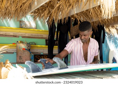 Focussed african american man preparing surfboard behind counter of surf hire beach shack. Local business, business owner, hobbies, sport, surfing, summer and vacation, unaltered. - Powered by Shutterstock