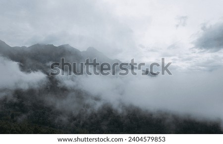 Fog and clouds in the mountains against the backdrop of the setting sun, changeable weather in the mountains, clouds and nebula on mountain peaks wide angle