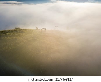 Fog envelops the mountain forest. The rays of the rising sun break through the fog. Aerial drone view.