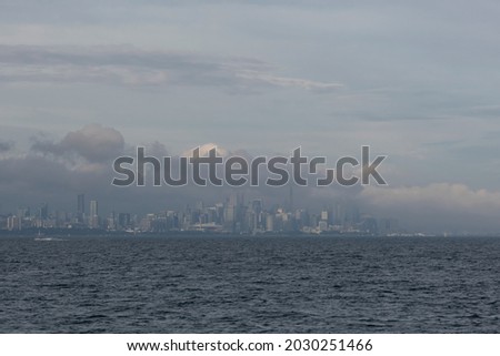 Fog and mist over lake Ontario water surface covers Toronto city skyline, heavy clouds on the sky. Weather conditions, advisory, alert concept. Space for copy.