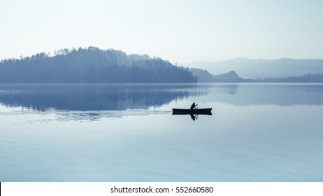 Fog over the lake. In calm water reflection mirror. Man with a paddle in the boat. Black and White. - Powered by Shutterstock