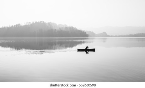 Fog over the lake. In calm water reflection mirror. Man with a paddle in the boat. Black and White