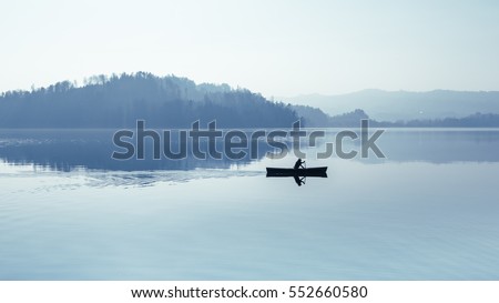 Fog over the lake. In calm water reflection mirror. Man with a paddle in the boat. Black and White.