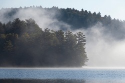 Fog Rolling In Over Blue Lake Between Pine Trees In Fall Near Muskoka, Ontario, Canada