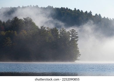 Fog rolling in over blue lake between pine trees in fall near Muskoka, Ontario, Canada