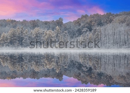 Foggy autumn landscape of the shoreline of Deep Lake flocked with snow and with mirrored reflections in calm water, Yankee Springs State Park, Michigan, USA