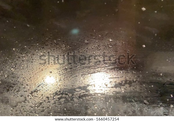 Foggy car window in snowfall winter day\
with traffic light and pedestrian in city road. Bad weather and\
storm with snowfall in city road, blur\
background