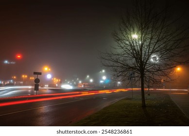 A foggy city street at night with car light trails, glowing streetlights, bare trees, and a quiet urban ambiance. Atmospheric and moody. - Powered by Shutterstock