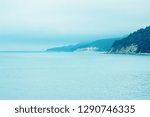 Foggy coastline with rocks and forests. Green hills on the beaches. Calm sea waters. You can see the sealine and the far distant, south horizon.  A photo with different, pleasant shades of blue.