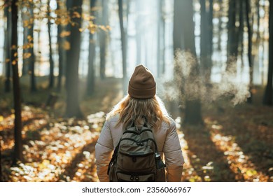 Foggy cold morning weather in autumn. Woman with backpack and knit hat hiking in forest at fall season