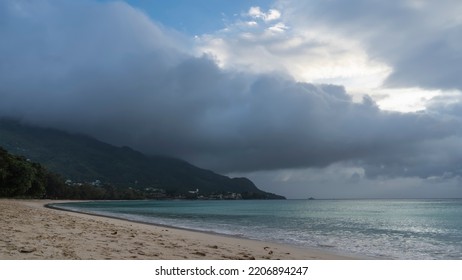 A foggy day on a tropical beach. The turquoise ocean is calm. Foam of waves on the sand. A rain cloud hung over the hill. Seychelles. Mahe. Beau Vallon - Shutterstock ID 2206894247