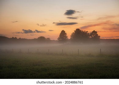 A foggy field with a fence and sunset