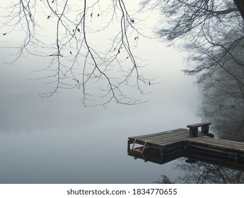 Foggy lake landscape with landing stage for boat. Lake, water and tree in the fog. Mystic trees under milky sky in the winter. Silent ambience. Germany, Brandenburg. Winter foggy landscape. Fog noir. - Powered by Shutterstock