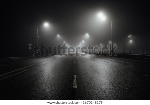 Foggy misty\
night road illuminated by street\
lights