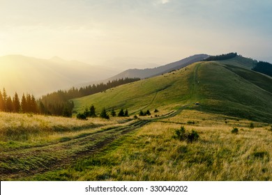 Foggy mountain road goes on top of the hills on sunset landscape. Sunbeams through the trees. - Powered by Shutterstock