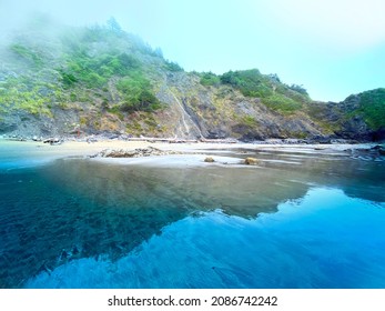 A Foggy Rainy Overcast Ocean Seashore Scene With Green Mountain Cliffs Waves