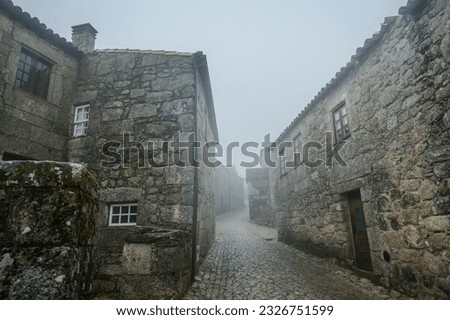 A foggy street in a Portuguese town, with stone houses and a stone road creating a captivating atmosphere.