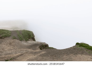 A foggy view of the Cliffs of Moher in County Clare, Ireland, with a rugged cliff edge disappearing into the mist. The overcast sky and fog obscure the ocean below, creating a mysterious ambiance - Powered by Shutterstock