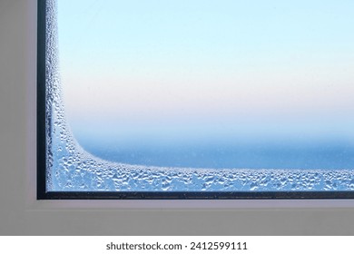 Foggy window glass covered with ice freezes indoors during severe frosts. Frozen defective plastic window in a room in winter.