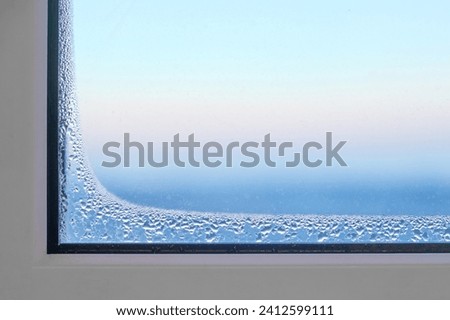 Foggy window glass covered with ice freezes indoors during severe frosts. Frozen defective plastic window in a room in winter.