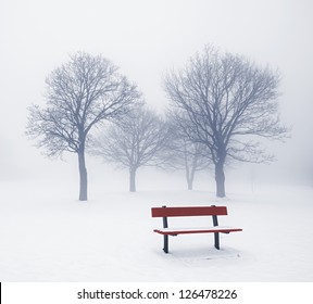 Foggy Winter Scene With Leafless Trees And Red Park Bench