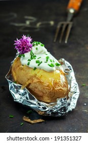 Foil Baked Jacket Potato Served In The Aluminium Foil Wrapper Topped With Sour Cream And Fresh Chopped Chives And Garnished With A Purple Chive Flower