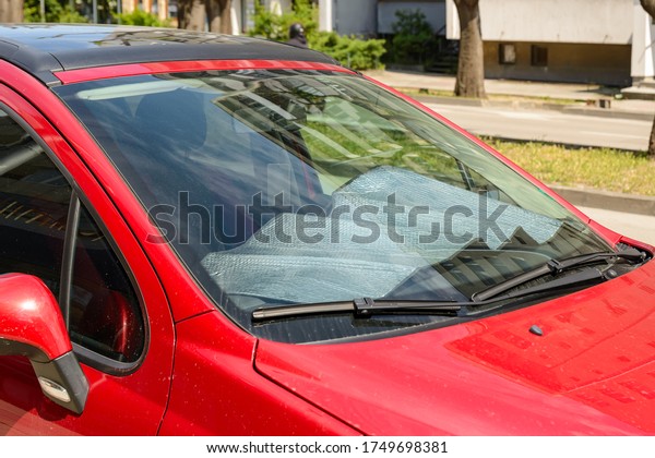 Foil sun shades covered a panel of a red car parked\
on the street on a sunny summer day. Reflective sun shield made of\
metallic silver foil protects vehicles from direct sunlight. Side\
view.