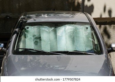 Foil Sun Shades Under The Windshield Of A Gray Car Parked Outdoors On A Sunny Summer Day. Reflective Sun Shield Made Of Metallic Silver Foil Protects Vehicles From Direct Sunlight. Front View.