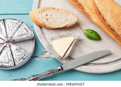 Foil Wrapped Processed Cream Cheese, Table Knife And Slice Of Bread On A Cutting Board Over Blue Wooden Table. Small Triangular Pieces Of Soft Cheese In An Aluminium Foil. Tasty Sandwich Ingredient. 