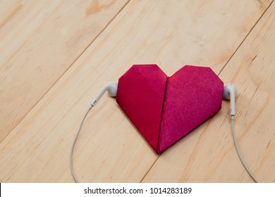 The fold red paper in heart shape with white headset on the wooden background. Listen to your heart concept.
