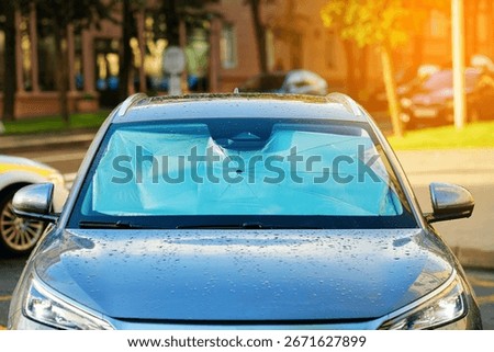 Foldable car windshield sunshade installed on parked car in sunny day. Car windshield sun shade protecting interior and dashboard from direct sunlight in parking lot. Protection from sunlight in car