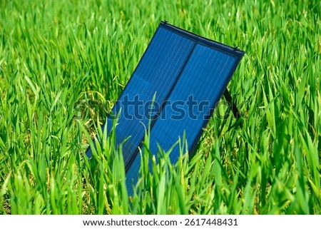Foldable portable solar panel placed in tall green grass, natural lighting, eco-friendly energy concept, renewable power in outdoor setting