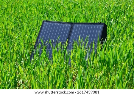 Foldable solar panel placed in tall green grass, natural lighting, eco-friendly energy concept, renewable power in outdoor setting