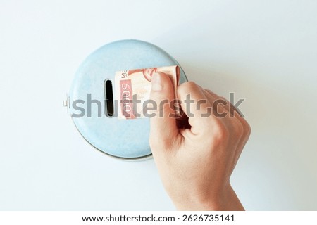 A folded 5000 ruble note in the hand of a Caucasian woman. Putting money into a metal bank piggy bank. White background.