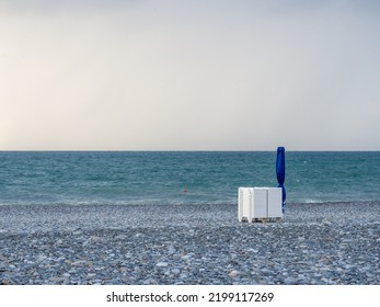 Folded Beach Umbrella And Sunbeds. End Of Beach Season. Not Bathing Time. High Wave. No People On The Beach
