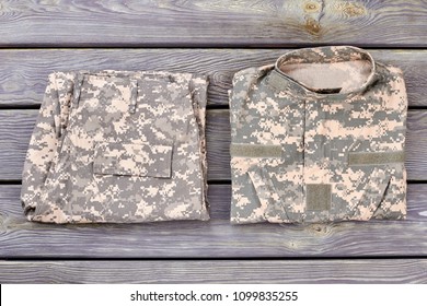 Folded Camouflage Jacket And Trousers. Wooden Desk Background.