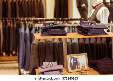 Folded classical shirts on the shelves, rows of men's suits hanging on the rack in the background