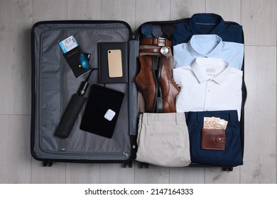Folded clothes, shoes and accessories in open suitcase on wooden background, top view. Packing for business trip