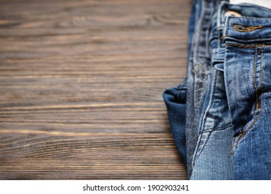 Folded denim pants on wooden background, place for text. Close-up.