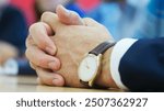 Folded hands of a man with a wristwatch on a table in an office during a meeting or negotiations. Unrecognizable businessman, lawyer or politician. Hidden emotions. Photo. Selective focus. Close-up