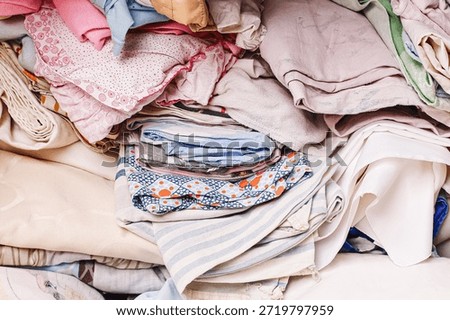 Folded laundry stack at home. Clean clothes sorted by color. Cotton fabrics and textiles pile. Household chores concept. Soft pastel clothing background. Domestic life organization and tidying scene.
