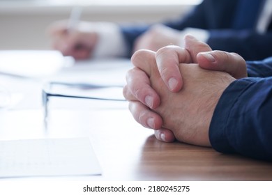 Folded male hands on a wooden table. Participant of negotiations, interviews, meetings. At the reception of a social worker, lawyer or employer. No face. Unrecognizable. Selective focus. Close-up - Shutterstock ID 2180245275