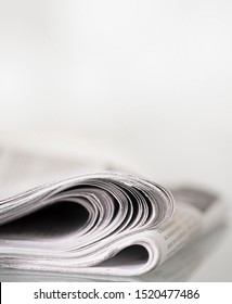 Folded Newspaper Mirrored On Glass Table Against Plain Light Background With Narrow Depth Of Field. Space For Text Above Newspaper